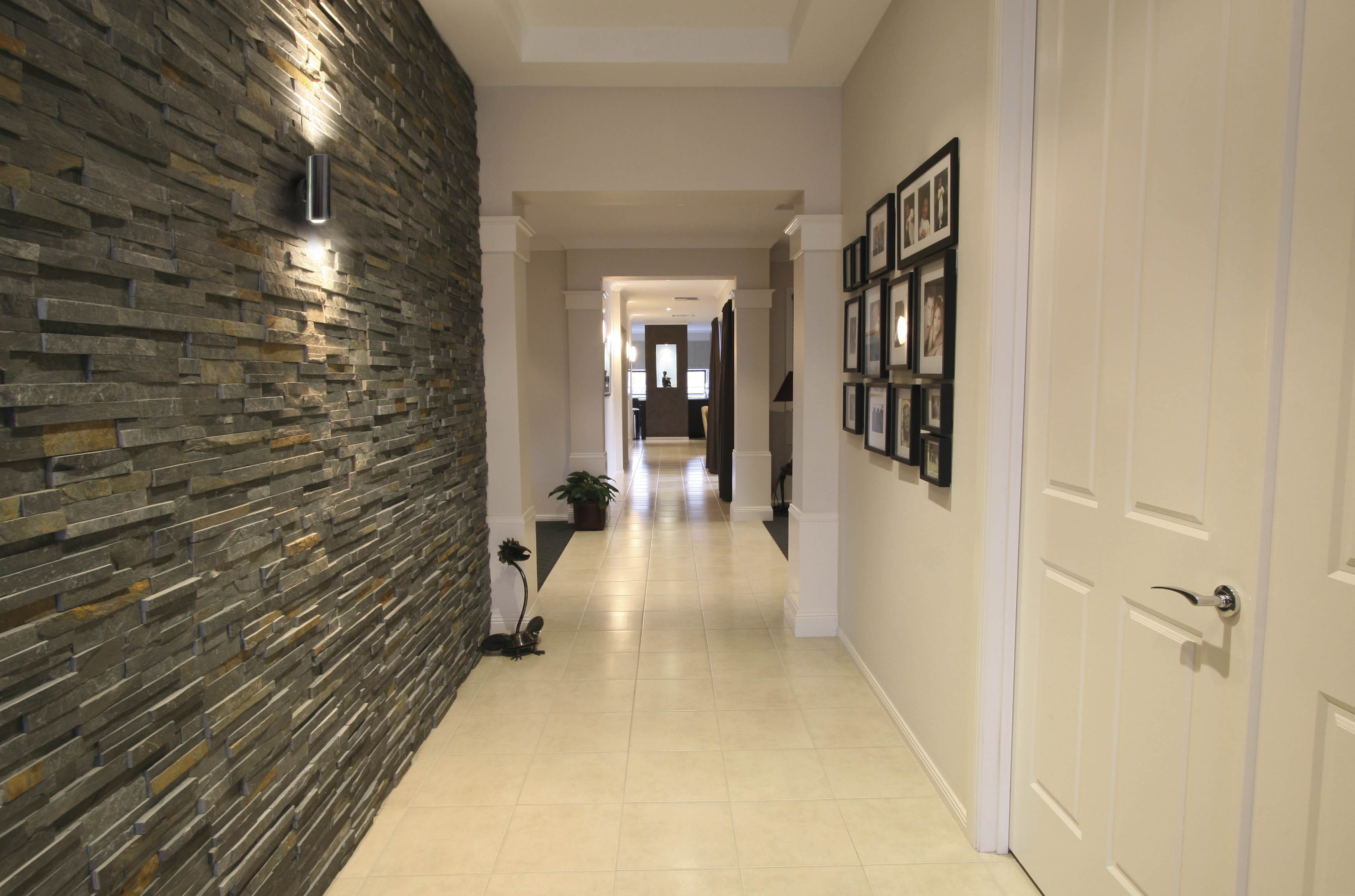 Looking down the hallway of a modern home with whote tiles for flooring and stoneword wall on left.